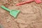 Red and green kids toddlers plastic play shovels laying on a sandbox sand background