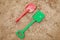 Red and green kids toddlers plastic play shovels laying on a sandbox sand background