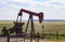 Red and grey and orange pumpjack on oil well in the plains with cattle grazing behind