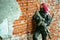 Red-hair airsoft woman in uniform with machine-gun, stand beside brick wall inside broken building. Horizontal background