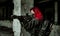 Red-hair airsoft woman in uniform with machine gun stand beside column. Closeup soldier aims at the sight stand inside of broken