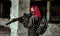 Red-hair airsoft woman in uniform with machine gun stand beside column. Closeup soldier stand inside of broken building,