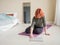 Red hair girl at home in bedroom. Woman sitting on yoga mat and opening laptop. Active lifestyle concept.