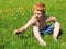Red hair little boy examines a yellow flower. Happy kid without a t-shirt, in denim shorts. Close up. Joyful, funny