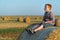 A red-haired boy sits on top of a straw bale on a wheat field