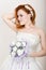 Red-haired bride in a wedding dress holding wedding bouquet, bright unusual appearance. Beautiful wedding hairstyle and