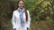 Red-haired Caucasian middle-aged woman in a white coat walks on a cloudy day in the autumn park