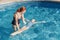 Red-haired Caucasian mother training daughter to swim in swimming pool outdoor. Mom teaching girl to swim and float on water.