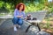 A red-haired curly girl in the park on a bench stroking a gray cat. Summer walk with the animal. Girl walking the cat