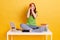 Red haired female wearing green t shirt and jeans sitting on table with crossed legs, being tired from learning, making spyglass