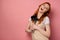 A red-haired girl in a apron stands on a pink background, joyfully opening mouth, clutching kitchen appliances to