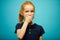 Red-haired girl covered her mouth with hand and looks at camera with concern over isolated blue background, expresses