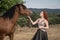 A red-haired girl feeds a brown horse and talks to it