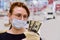 A red-haired girl in a medical mask stands with dollars in her hands near the store cash register