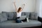 A red-haired girl sits on a sofa in home clothes with a laptop on crossed legs and stretches her arms to the sides