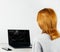 Red-haired girl sitting at a table and looking at a laptop with a broken, cracked screen.