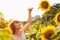 Red-haired girl is standing next to a tall sunflower, a woman measures the height of a sunflower, her hand is lifted up