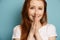 Red-haired girl in a white T-shirt stands on a blue background and smiles while holding folded palms in front of her