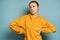 A red-haired girl in a yellow sweatshirt stands on a blue background, looks to the side, putting his hands on his belt.