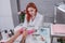 The red-haired manicurist sits at the work table in the salon, holds the client`s hands and examines them.