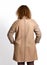 Red-haired model woman poses with her back to us in stylish beige sheepskin coat combined with textile sleeves