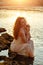The red-haired sensual girl in white dress sitting on the rocks