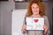 Red haired smiling businesswoman holding small poster.