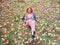 Red-haired smiling girl sits in a meadow strewn with autumn maple leaves