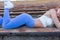 A red-haired sportswoman, showing her figure, does a warm-up before playing sports, lying on a bench of a football stadium. active