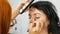 Red-haired stylist make-up artist doing stylish evening make-up of model with long black hair in beauty salon