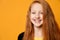 Red-haired teenage kid in black jacket. She is smiling and looking at you, posing against orange studio background. Close up