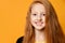 Red-haired teenage kid in black jacket. She is smiling and looking at you, posing against orange studio background. Close up