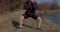 Red-haired woman doing body workout city park holds pose crouches down stands up