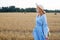 A red-haired woman in a hat and a blue dress walks in a field with haystacks.