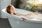 Red-haired woman relaxing in bathtub with foam in spa center.