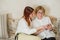 Red-haired woman teaches an elderly mother how to use a smartphone. Mother and adult daughter dressed in white blouses are sitting