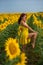 A red-haired woman in a yellow dress is standing in a field of sunflowers. Beautiful girl in a skirt sun enjoys a cloudless day in