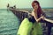 Red haired womanstanding in the sea water leaning on the pier. Mermaid coming out of water and trying to make first steps