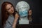 Red-haired young girl on a black background a gray t-shirt, wears a protective medical mask on white antique plaster bust head