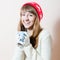 Red hat & cup: portrait of pretty girl in knitted gloves and cap with a pattern snowflakes, white sweater having hot drink