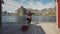 red head girl runs on the pier towards the sea next to the traditional red wooden rorbu fisherman's house on the