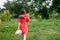 Red head teen girl in dress walks back to the camera with shovel on shoulder and hat in her hand, people and garden