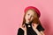 Red-headed teenager in black dress and red hat. She kissing you, holding on to choker, posing on pink studio background. Close up