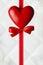 Red heart, bow and ribbon on white quilted leather background