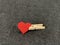 Red heart clamped clothespin, on a dark background. Sign of the heart in slavery. Concept: heart disease, addiction