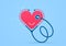 Red heart with doctor`s stereoscope on a blue background. Health care and healthy lifestyle concept. Cardiac help, heartbeat puls