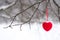 Red heart hanging on red thread on tree branch in winter in snowfall focus partial blurred background