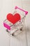 Red heart in a mini supermarket trolley on a white wooden table.