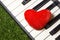 Red heart on piano, grass background