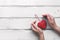 Red heart on a ribbon and female hands, white wooden plank background. Valentine`s Day.Top view, copy space